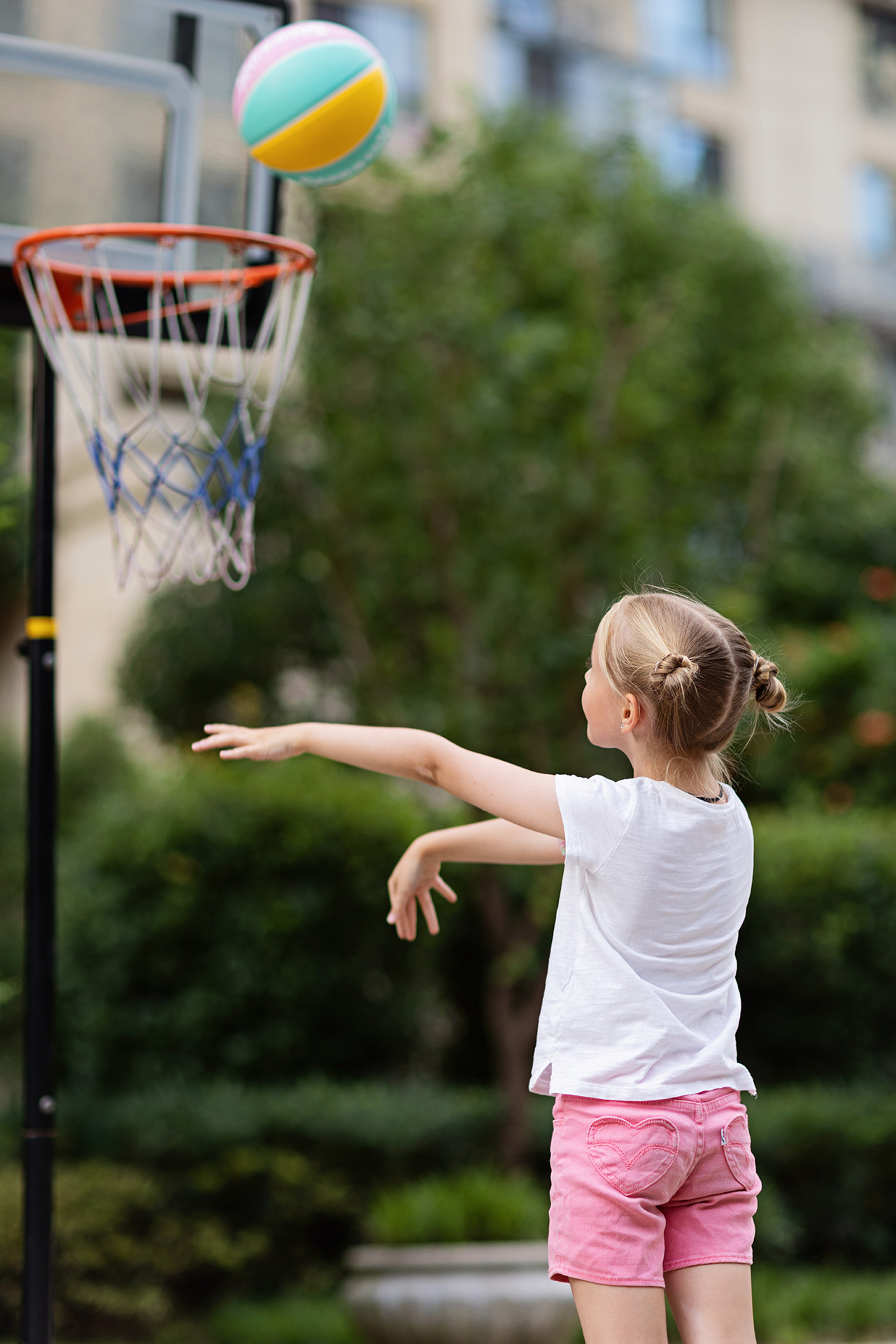Candid lifestyle portrait of happy Cheerful caucasian little girl with blonde hair seven years old holding game ball for basketball outdoor at hot summer day. High quality photo